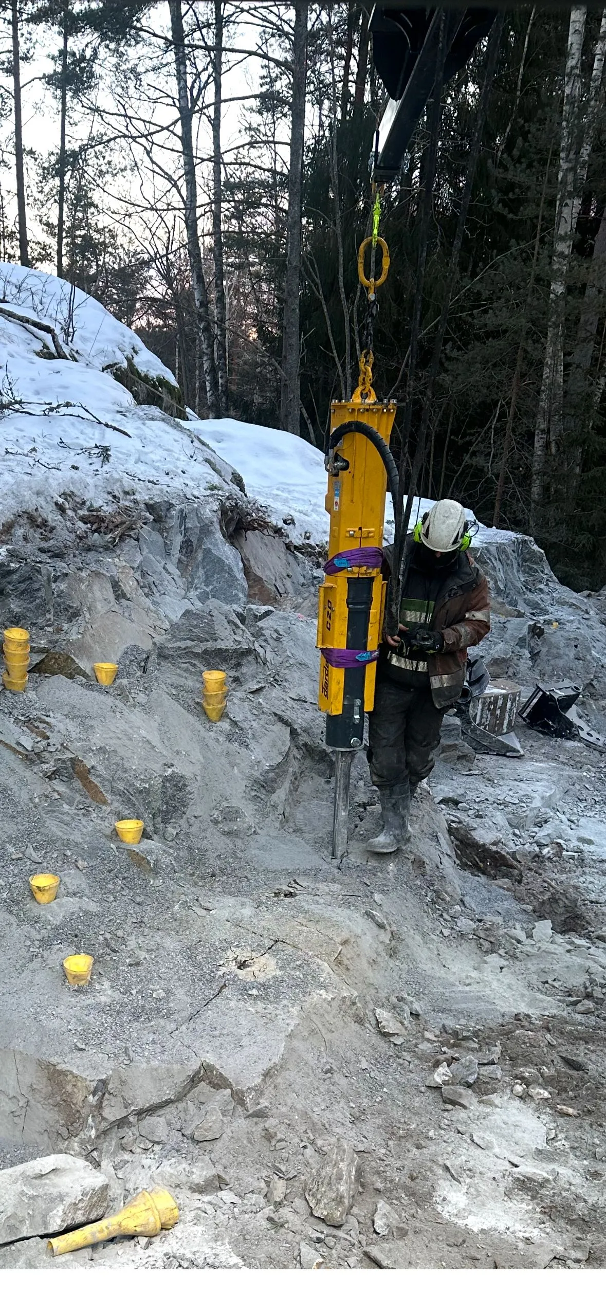 Stor gul Darda C20 upphängd i kätting vid bergarbete med markerade borrhål.