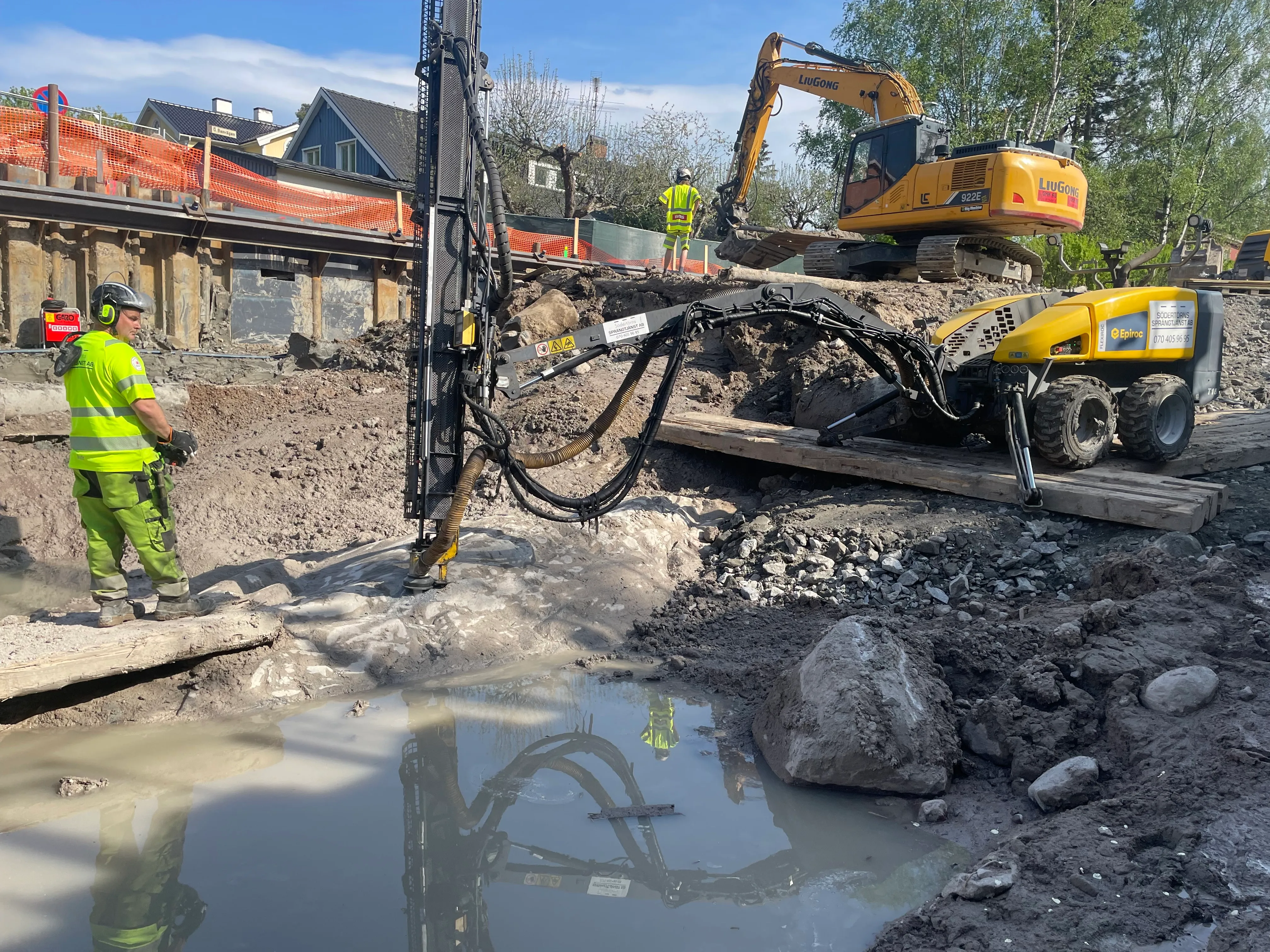Bergschakt i gatumiljö med borrigg och grävmaskin